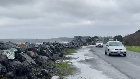 Cars-travel-on-beach-road-with-water-splashing-over-the-rocks-during-strong-storm
