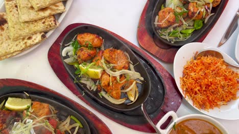 Traditionelles-Indisches-Tandoori-Huhn-Mit-Zwiebeln-Auf-Einer-Sehr-Heißen-Platte-Mit-Dampfrauch,-Butterhuhn,-Käse-Naan-Brot-Und-Kokosreis-In-Einem-Restaurant,-Authentische-Asiatische-Küche,-4k-Aufnahme