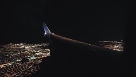 Plane-landing-in-an-airport-next-to-a-city-at-night-from-the-inside-looking-outside-at-the-wing