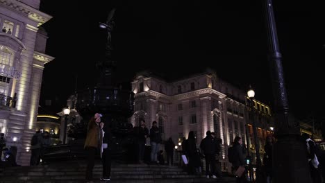 Couple-standing-in-central-piccadilly-circus-in-front-of-fountain-taking-a-selfy-at-night