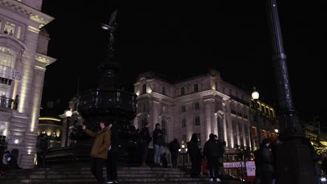 Couple-standing-in-central-piccadilly-circus-in-front-of-fountain-taking-a-selfy-at-night