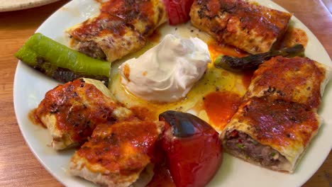 Traditional-Turkish-Gozleme-meat-dish-with-sour-cream,-delicious-beef-stuffed-pancake-with-roasted-tomatoes-and-peppers,-authentic-food-on-a-plate-in-Bodrum-Turkey,-4K-shot