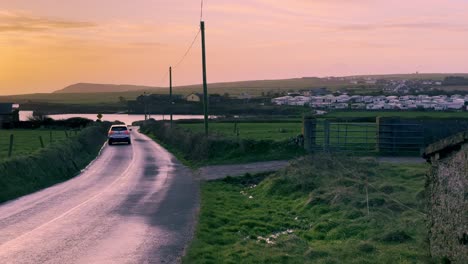 Early-morning-in-winter-with-sun-rising-over-ocean-and-car-passing-on-rural-road-in-Ireland