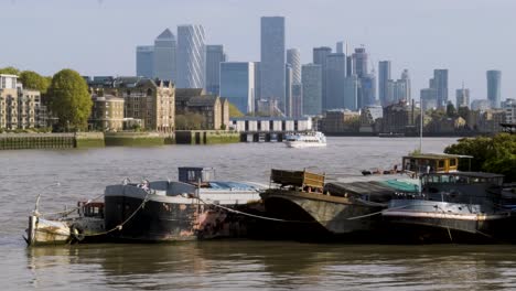 Wide-shot-of-boats-docked-on-river-thames-with-view-of-Canary-Wharf-skyscrapers-on-a-sunny-summer-day-with-clear-skies