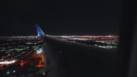 Plane-landing-in-an-airport-next-to-a-city-at-night-from-the-inside-looking-outside-at-the-wing