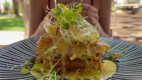 Girl-taking-photos-for-social-media-of-a-delicious-breakfast-brioche-toast-with-poached-eggs,-smoked-salmon-and-smashed-avocado-with-hollandaise-sauce,-female-enjoying-brunch-in-a-restaurant,-4K-shot