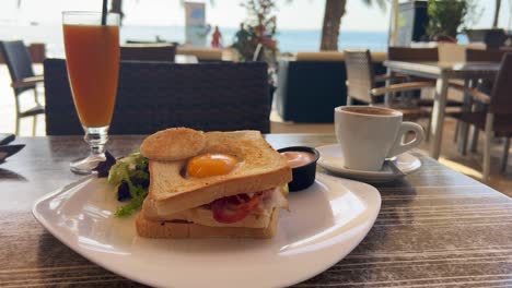 Classic-breakfast-sandwich-with-egg,-bacon-and-salad-with-fresh-orange-juice-and-coffee,-morning-brunch,-4K-shot