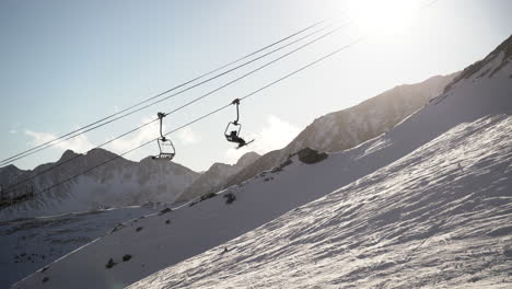 Skiliftstühle,-Die-Auf-Kabeln-Den-Schneebedeckten-Berg-Hinauffahren,-Der-Sich-Durch-Helles-Sonnenlicht-Bewegt