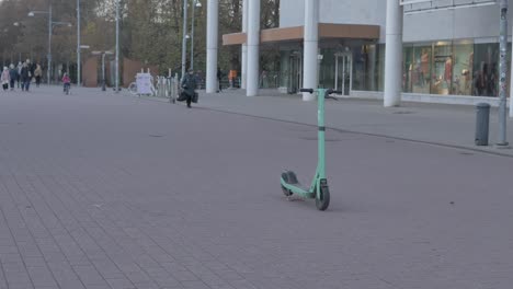 people-are-walking-on-background-in-slow-motion,-behind-of-green-bolt-electric-scooter