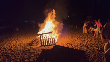 Traditional-bonfire-festival-at-the-beach-at-the-San-Juan-celebration-in-Marbella-Spain,-people,-friends-and-family-enjoying-a-fun-party-during-summer,-big-burning-fire-and-hot-flames,-4K-shot