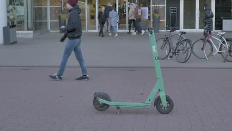 people-are-walking-by-in-slow-motion-of-green-bolt-electric-scooter,-Bolt-has-been-parked-middle-of-pedestrian-street