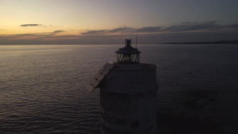 Striking-Lighthouse-shining-light-at-sunset,-aerial-drone-circling-around