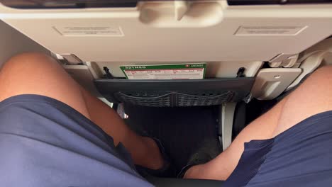 Traveling-in-tight-airplane-seat-with-very-little-legroom-space,-male-legs-and-knees-squeezed-tight-on-a-Turkish-airlines-aircraft,-uncomfortable-airline-seat,-4K-shot