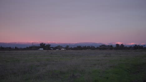 A-pastel-sky-over-the-Sierra-Nevada-mountains-with-power-lines-and-a-farm,-in-the-foreground-in-Clovis,-CA,-USA