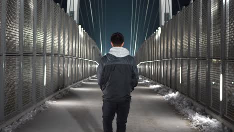 Young-white-male-walking-away-from-camera-on-a-pedestrian-bridge-at-night