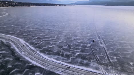 A-truck-is-followed-by-a-aerial-drone-across-the-frozen-Lake-Invermere-in-British-Columbia,-Canada
