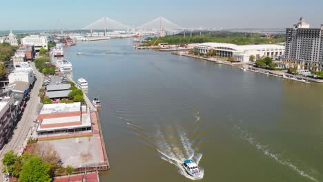 Aerial-view-of-boat-moving-on-the-savannah-river-with-buildings-lined-up-of-both-sides-of-the-river-banks