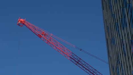 red-arm-of-a-crane-in-sunlight-moves-next-to-skyscraper-window-front