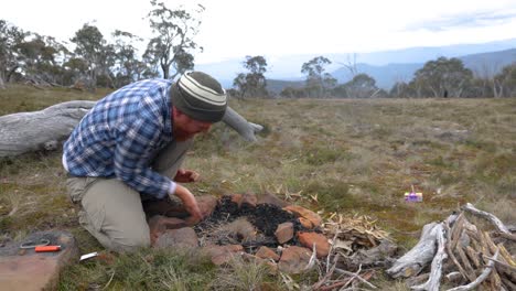 A-man-blows-on-a-tinder-buddle-to-get-a-fire-going-in-the-Australian-mountains