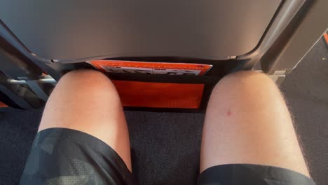 Traveling-in-tight-airplane-seat-with-very-little-legroom-space,-male-legs-and-knees-squeezed-tight-on-an-Easyjet-aircraft,-uncomfortable-airline-seat,-4K-shot