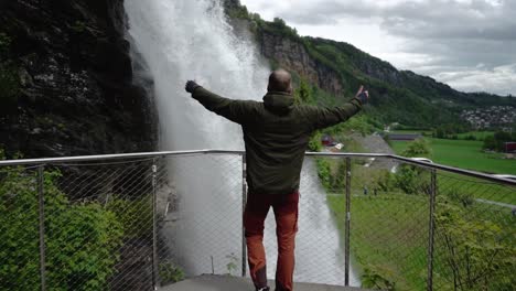 Slow-motion-shot-of-man-raising-arms-in-front-gigantic-waterfall-in-Norway---Slow-motion