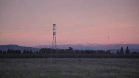 A-pastel-sky-over-the-Sierra-Nevada-mountains-with-power-lines-and-trees,-in-the-foreground-in-Clovis,-CA,-USA