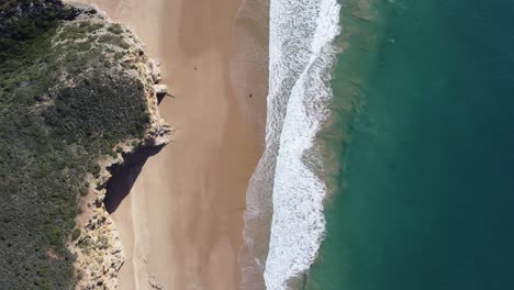 waves-rolling-at-the-beach-of-beliche,-beautiful-water-colors,-sunny-droneshot-from-above