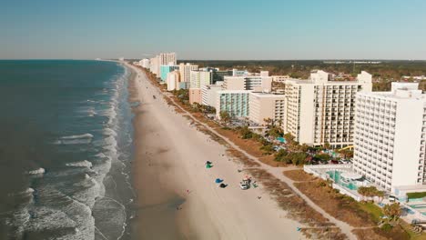 Aerial-view-of-Myrtle-Beach-with-resorts-lined-up-at-the-beach-front-and-waves-gently-crashing-at-shore