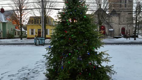 Toma-Aérea-Lenta-De-Un-árbol-De-Navidad-Decorado-Que-Revela-La-Iglesia,-Las-Casas-Y-La-Hermosa-Luz-Dorada-De-La-Hora-Dorada-En-Un-Día-Cubierto-De-Nieve-En-Wellsboro-Pa