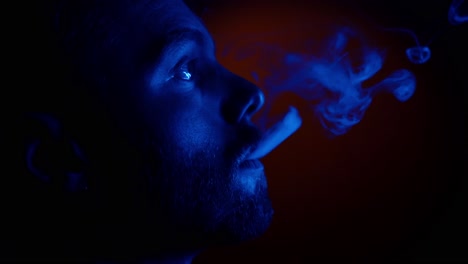 Close-up-shot-of-man-smoking-cigarette-in-dark-room-with-blue-flashing-light-in-studio---Unhealthy-lifestyle