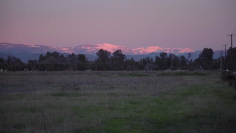 A-pastel-sky-over-the-Sierra-Nevada-mountains-with-power-lines-and-trees,-in-the-foreground-in-Clovis,-CA,-USA