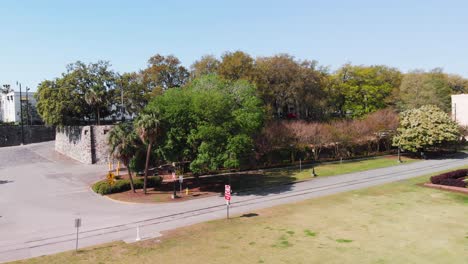 Die-Drohne-Erhebt-Sich-über-Einem-Grünen-Parkgelände-Mit-Vielen-Bäumen-Und-Straßenverkehr-Im-Hintergrund