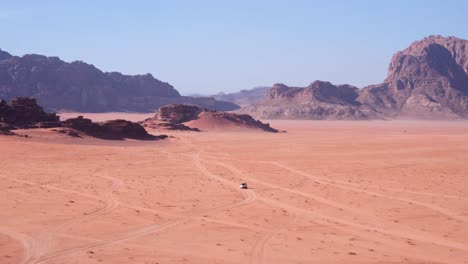 White-4WD-truck-driving-across-Wadi-Rum-desert-in-Jordan,-near-the-border-of-Saudi-Arabia,-remote,-vast-red-sandy-landscape