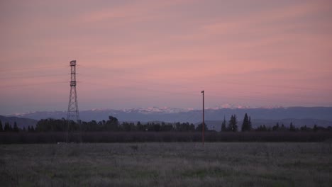 A-pastel-sky-over-the-Sierra-Nevada-mountains-with-power-lines-and-a-field-in-the-foreground-in-Clovis,-CA,-USA