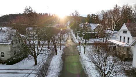 Slow-aerial-dolly-forward-in-towards-bright,-warm-sunshine-in-snow-covered-neighborhood-in-America