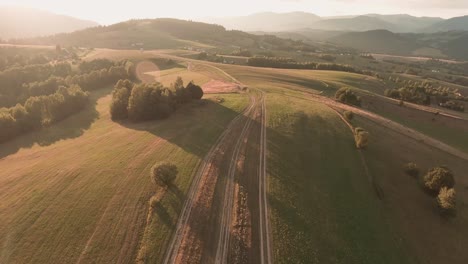 Aerial-footage-from-a-racing-drone-following-an-unpaved-road-in-a-beautifully-sunlit-mountain-scenery-with-trees-casting-long-shadows