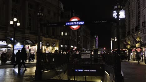 People-walking-at-night-next-to-entrance-to-Public-Subway-Underground-Station-Piccadilly-Circus-in-London-Downtown