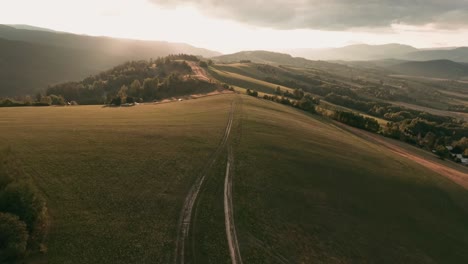 Aerial-racing-drone-following-an-unpaved-road-in-a-beautifully-sunlit-mountain-scenery-with-trees-casting-long-shadows