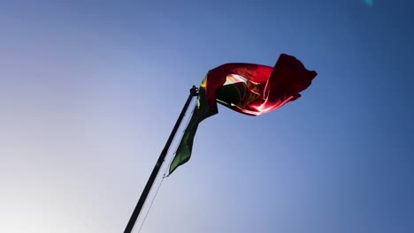 Slow-motion-view-of-the-flag-of-Portugal-flying-against-a-blue-sky-background-on-sunny-day
