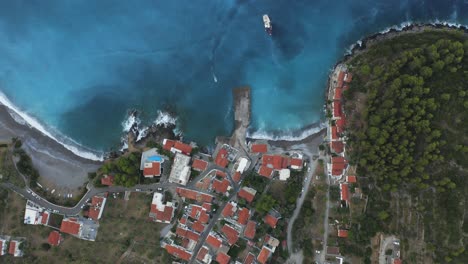 A-birds-eye-view-of-a-coastal-village-in-Lakonia,-Greece-with-a-small-boat-approaching