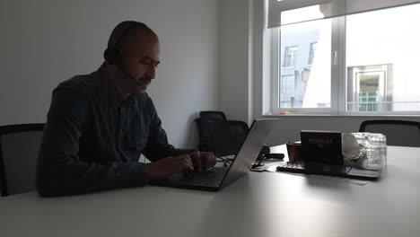Bald-Male-Freelancer-Wearing-Headset-Talking-Through-Laptop-In-Meeting-Room