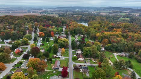 High-descending-aerial-of-neighborhood-surrounded-by-colorful-forest,-woodlands-during-autumn