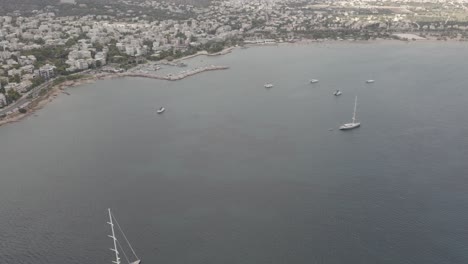 An-aerial-reveal-of-a-coastal-city-from-the-sea-with-various-sailboats-in-the-foreground