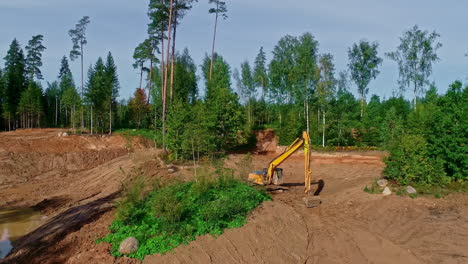 Heavy-digger-working-on-water-pond-in-forestry-area,-aerial-view