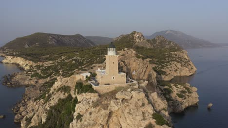 A-point-of-interest-rotational-drone-shot-of-a-lighthouse-in-the-edge-of-some-high-cliffs,-with-the-greek-flag-on-one-side