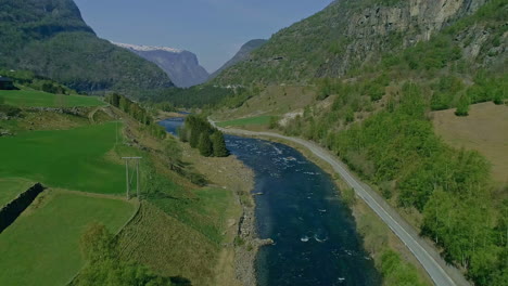 Luftaufnahme-Des-Blauen-Flusses,-Umgeben-Von-Begrünten-Bergen-Und-Schneebedeckten-Gipfeln-Im-Hintergrund---Sommerzeit-In-Norwegen,-Europa