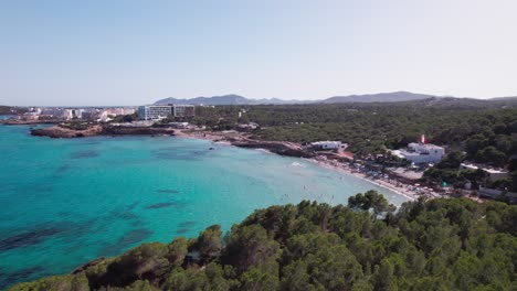 Vuelo-Aéreo-Sobre-Una-Hermosa-Playa-En-Un-Día-Soleado-Con-Agua-Azul-Y-árboles-Verdes-En-Ibiza