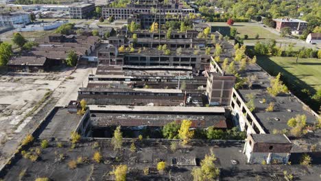 Old-Packard-Plant-building-overgrown-with-green-trees,-aerial-drone-view
