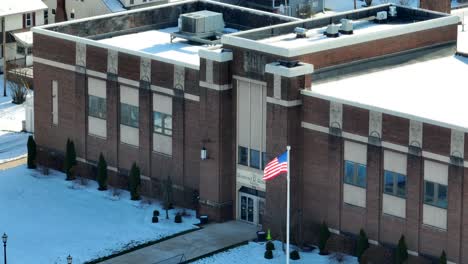 Tight-aerial-zoom-of-American-flag-waving-in-front-of-brick-school
