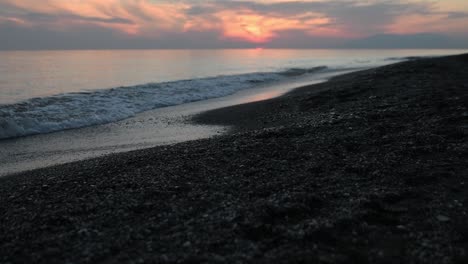 Serene-slow-motion-gravel-beach-at-sunset-with-tranquil-waves-at-low-tide